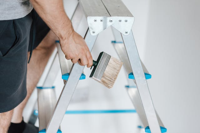 man holding a paint brush on a ladder